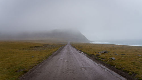 Road amidst land against sky during foggy weather