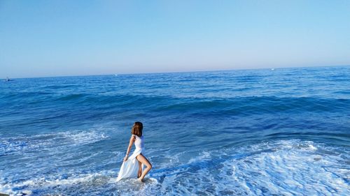 Side view of young woman standing in sea against clear blue sky