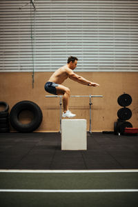 Full length of shirtless man sitting on wall