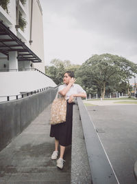 Full length of woman standing by railing on road against sky