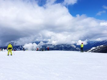 People skiing on snowcapped mountain against cloudy sky