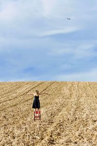 Rear view of woman with arms outstretched standing on land against sky