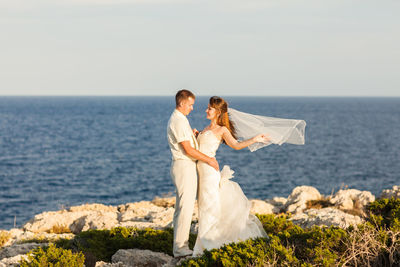 Couple kissing on rock by sea against sky