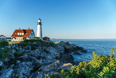 Lighthouse amidst sea and buildings against sky