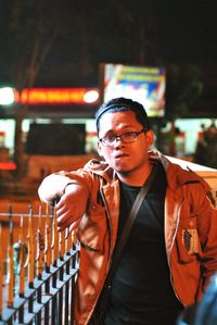 Portrait of young man wearing jacket by railing at night