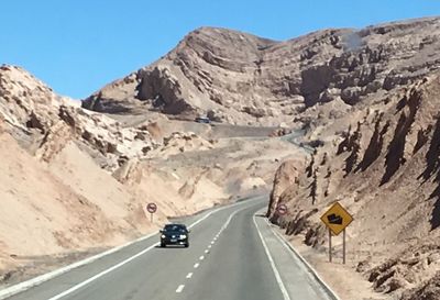 Road passing through rocky mountains against clear blue sky