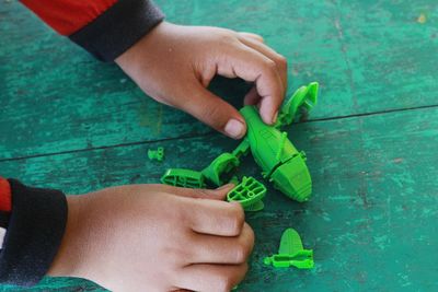 Cropped hands of child playing with green toy at table