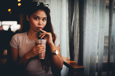 Portrait of young woman drinking iced coffee in cafe