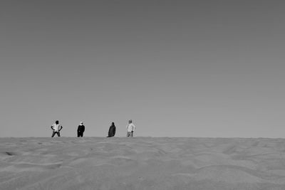 People on sand dune against clear sky