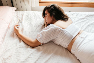 High angle view of young woman using phone while lying on bed at home