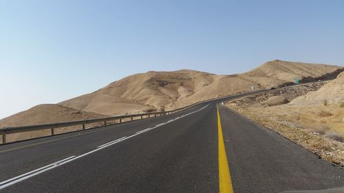 Empty road amidst mountains against clear sky on sunny day