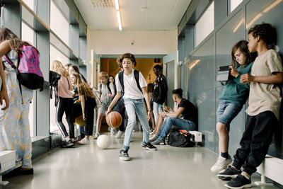 Male student playing with basketball during lunch break in school corridor