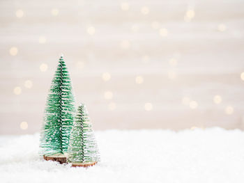 Christmas trees in  foreground in artificial snow and blurred background with glowing garland. 