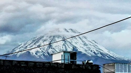 Low angle view of snow covered mountain against cloudy sky