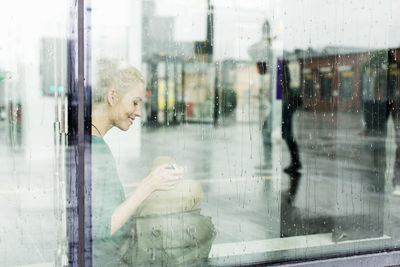 Young woman sitting on sill seen through glass at railroad station
