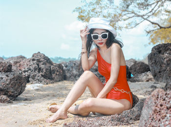 Young woman wearing sunglasses sitting on rock at beach