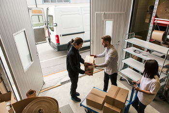 High angle view of male coworkers delivering boxes while female is using digital tablet