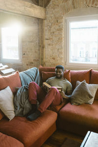 Young man reading book while relaxing on sofa at home