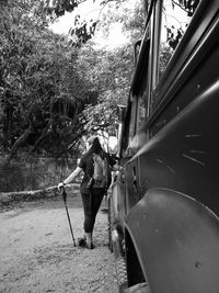 Rear view of woman with hiking pole leaning on vehicle