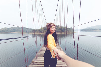 Cropped image of couple with holding hands on bridge over river against sky