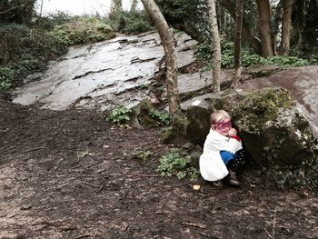 Smiling girl sitting by rock in forest