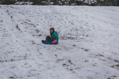 Full length of girl sitting on bobsled in snow