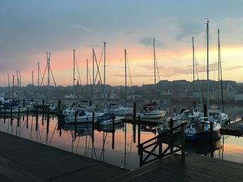 Sailboats moored in harbor at sunset