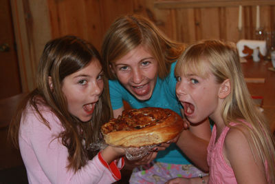 Portrait of happy sisters eating cinnamon roll at home