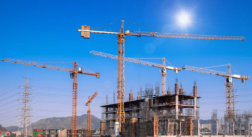 Low angle view of cranes against blue sky