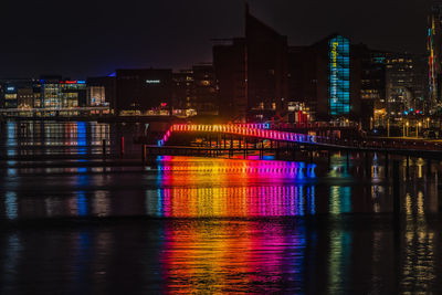 Illuminated buildings by river against sky at night