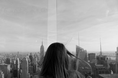 Rear view of woman looking at modern buildings in city against sky
