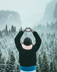 Rear view of man making heart shape during snow fall
