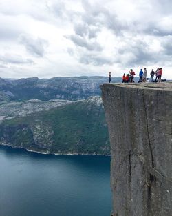 Tourists standing on cliff by sea against cloudy sky