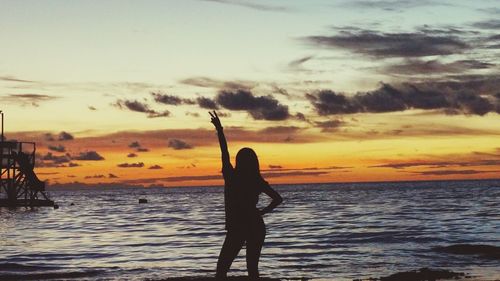 Silhouette woman standing on beach against sky during sunset