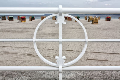 Hooded chairs at beach seen through white railing