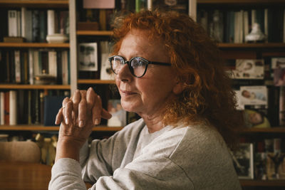 Thoughtful senior woman with hands clasped sitting at home