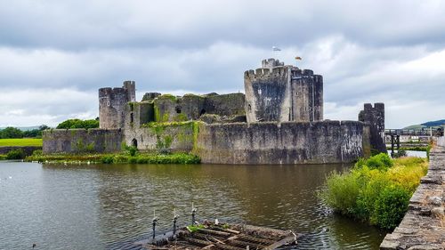 Caerphilly castle by lake against cloudy sky