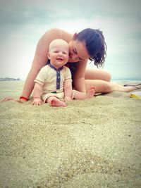 Mother with smiling toddler on sea shore at beach against sky