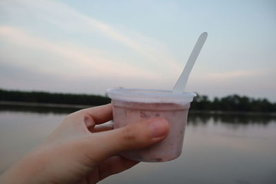 Midsection of person holding ice cream against lake