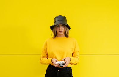 Close-up of a smiling young caucasian woman on a yellow background holding a photo camera
