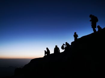 Silhouette people on rock against sky during sunset