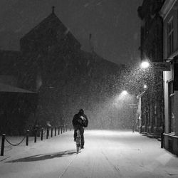 Man cycling on snow covered road towards building at night