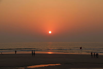 Silhouette people on beach against clear sky during sunset