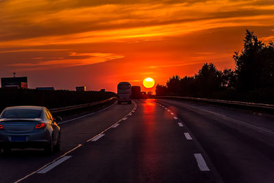 Cars on road against orange sky during sunset