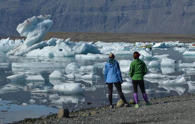 Rear view of women standing by frozen lake during winter