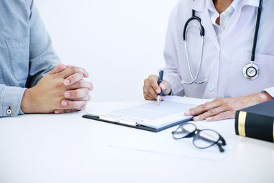 Midsection of doctor writing prescription while worried patient sitting at table