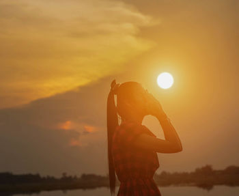 Side view of silhouette woman standing against orange sky