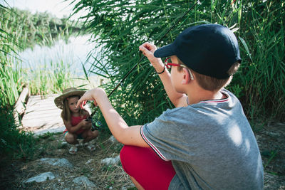 Cute sister holding fishing rod while brother crouching on field