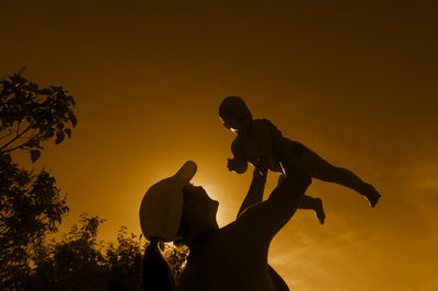 Low angle view of father holding toddler daughter against orange sky