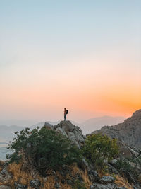 Man standing on rock against sky during sunset